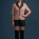 Woman wearing a pink blazer with black lapels, black shorts, and black knee-high boots on a blue background